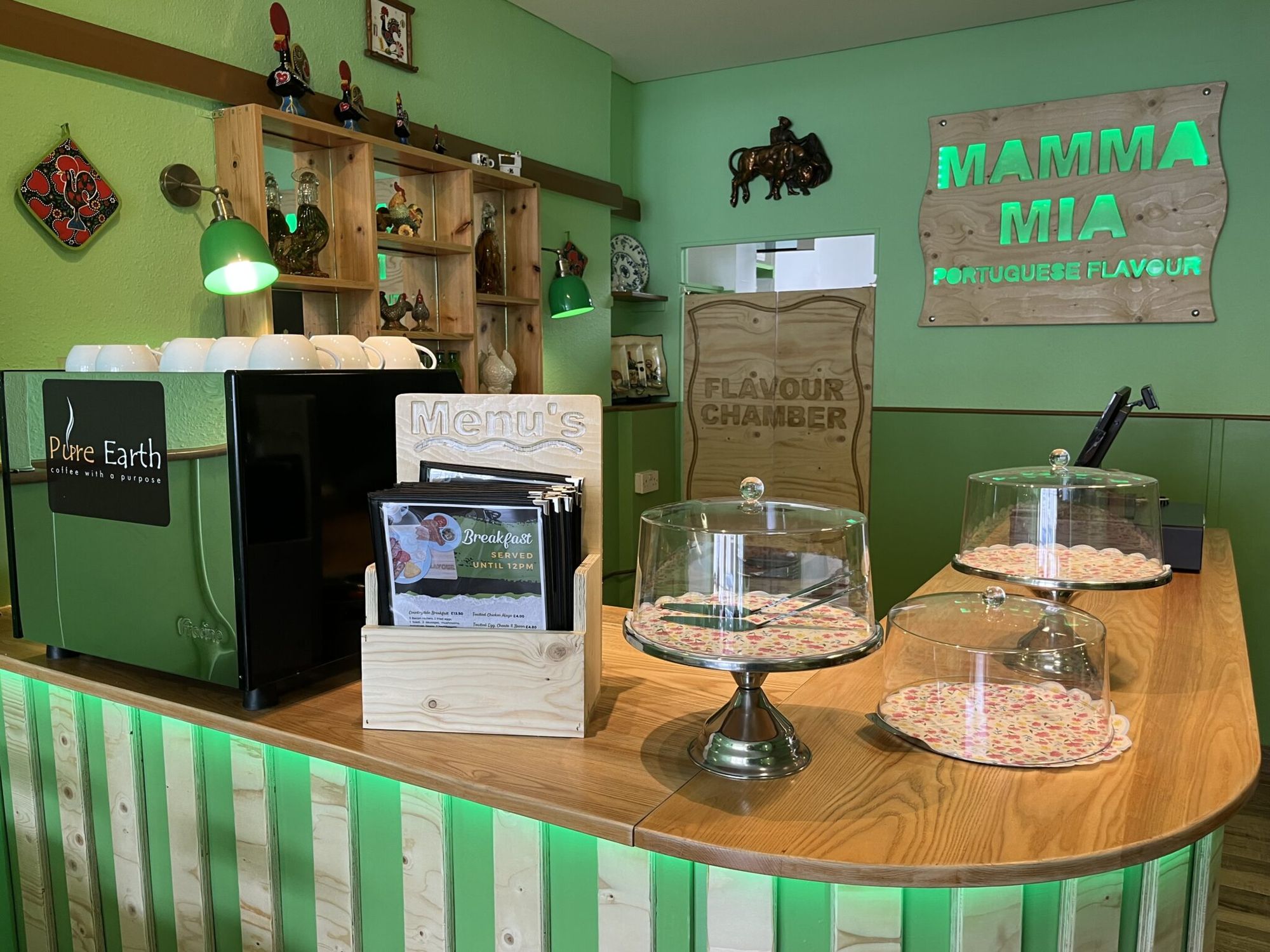 Inside Mamma Mia: the bar under the glowing green sign, lined with Portuguese rooster ornaments