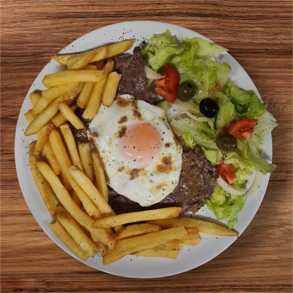 Beef prego plate topped with a fried egg, chips and Portuguese salad